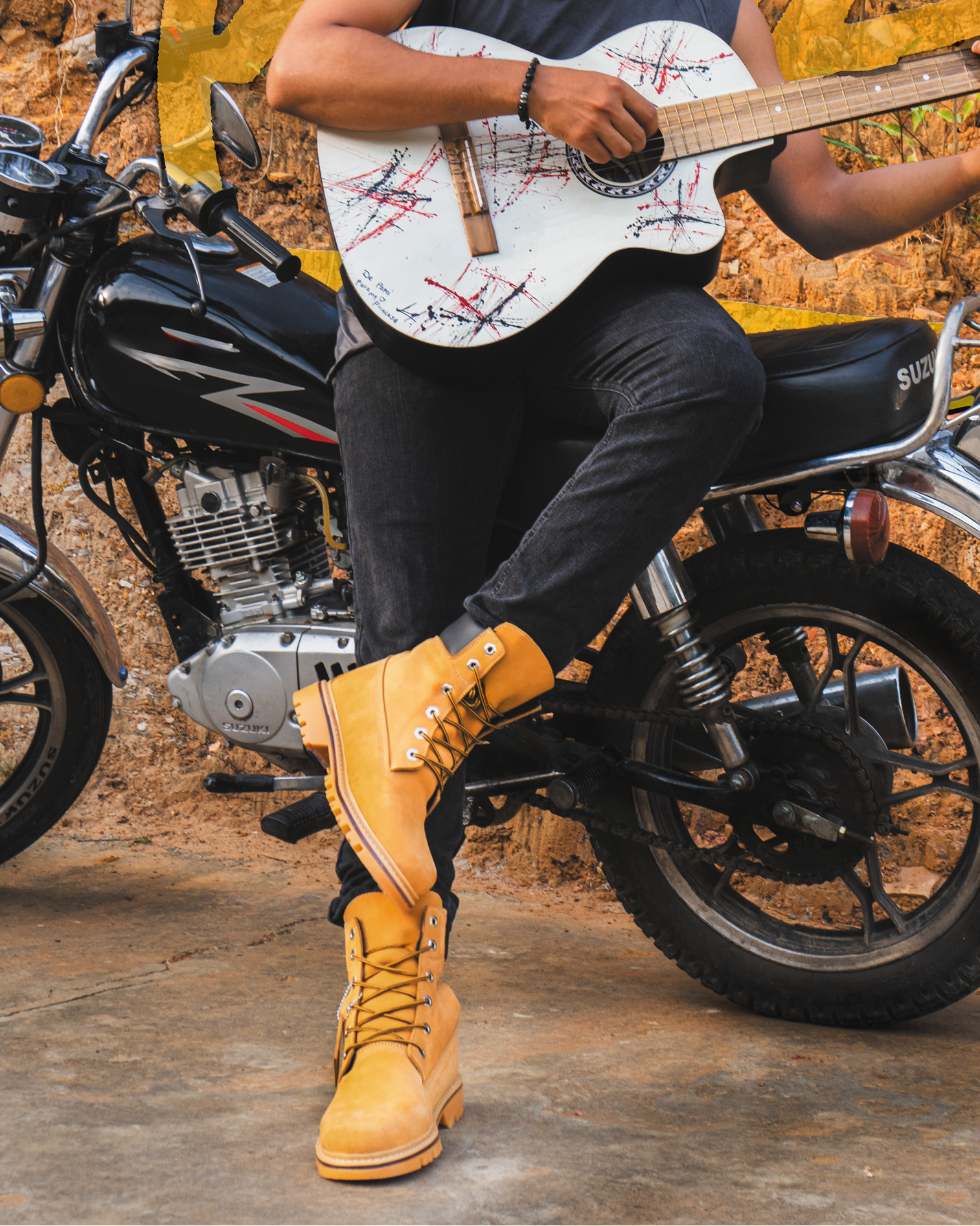 Man playing a guitar on a motorcycle with a decorative wall in the background